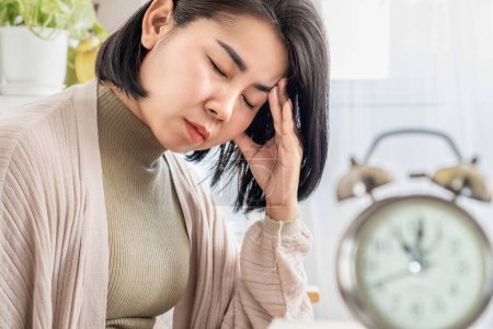 Photo for Asian woman suffering from chronic daily headache with alarm clock in foreground - Royalty Free Image