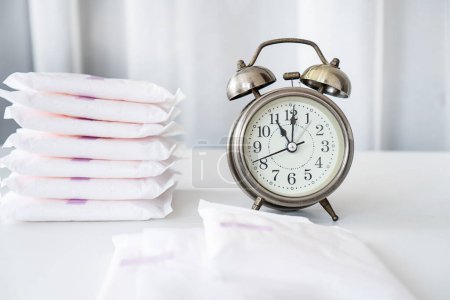 Photo for Changing Pads, don't wear a pad  too long concept with an alarm clock and menstrual pads on the table can be used for irregular periods concept - Royalty Free Image