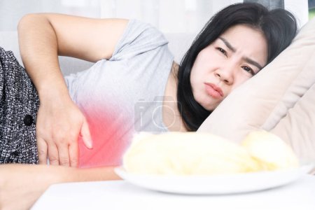 Téléchargez les photos : Femme asiatique couchée après avoir mangé cause de l'inconfort, de l'indigestion avec de l'acide gastrique ou un RGO - en image libre de droit