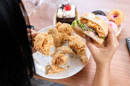 Photo for Unhealthy woman eating fast food burgers, fried chicken, donuts and desserts, binge eating disorder concept - Royalty Free Image