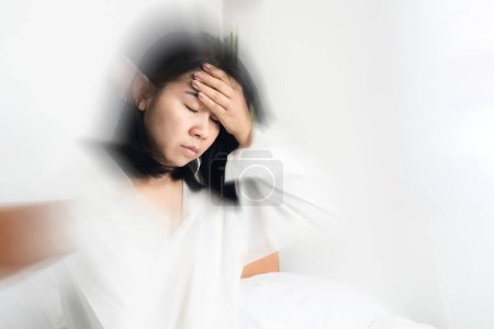 Mujer asiática desmayándose, mareos después de despertarse en la cama mano sosteniendo su dolor de cabeza