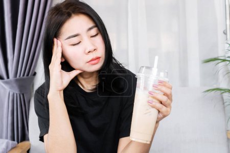 Photo for Asian woman having a headache and dizzy after drinking ice coffee, headache triggered by caffeine concept - Royalty Free Image