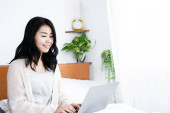 Asian business woman working from home sitting in bed had typing on laptop t-shirt #658400998