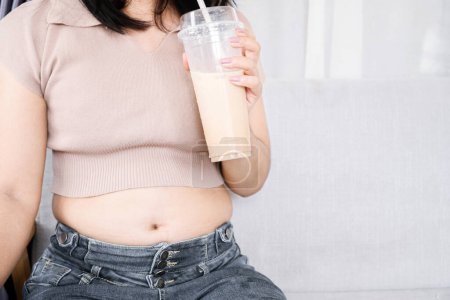 Téléchargez les photos : Grosse femme avec gros ventre boire du thé au lait, boisson sucrée, concept de dépendance au sucre - en image libre de droit
