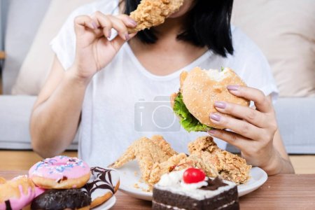 Binge concept de trouble de l'alimentation avec femme manger hamburger de restauration rapide, poulet cuit, beignets et desserts