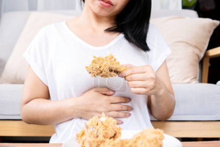 Asian woman overeating fried chicken have a stomachache, indigestion because of eating too much, or binge eating disorder