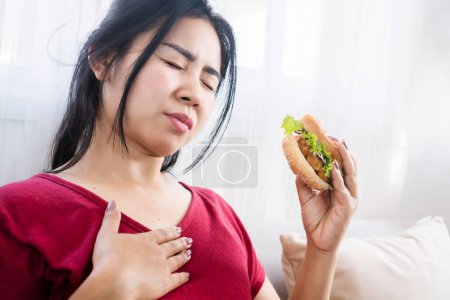 Mujer asiática con acidez estomacal, reflujo ácido después de comer hamburguesa, comer concepto de comida chatarra