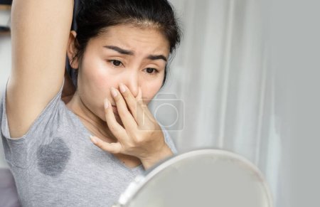 Foto de Mujer asiática oliendo su apestosa y sudorosa axila y mirando un espejo - Imagen libre de derechos