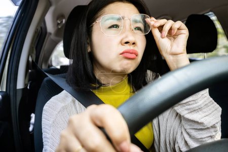 Photo for Forbidden and perilous concept with Asian woman struggles to drive due to blurry vision, hand clutching eyeglasses, and prohibited driving - Royalty Free Image