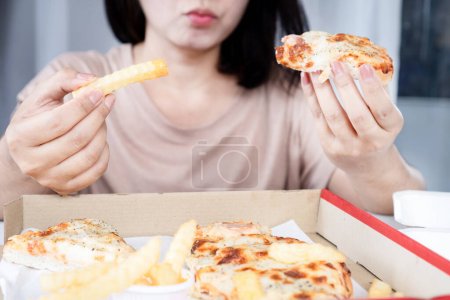 Mujer asiática comiendo en exceso pizza y papas fritas, estilo de vida poco saludable, atracones concepto de trastorno alimenticio