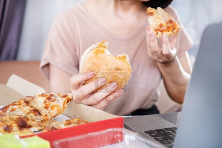 Binge Eating Disorder Konzept mit Frau über das Essen von Fast Food Burgern und Pizza am Schreibtisch