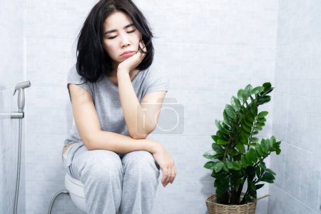 Foto de Mujer asiática tiene problemas con hipersomnia sensación de sueño todo el tiempo, fatiga crónica, sentarse y dormir en el baño - Imagen libre de derechos