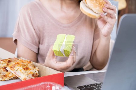 Frau isst Fast-Food-Burger, Pizza und Desserts am Schreibtisch, Essstörungskonzept 