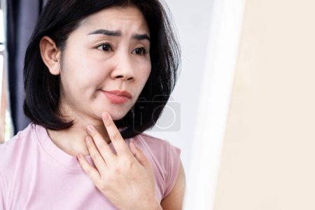 Femme asiatique ayant un problème avec la paralysie de Bell, paralysie faciale, main tenant son visage devant un miroir 