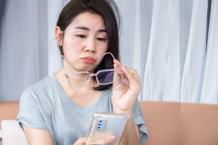 Femme asiatique ont flou vision main tenant des lunettes essayer de lire écran de téléphone mobile