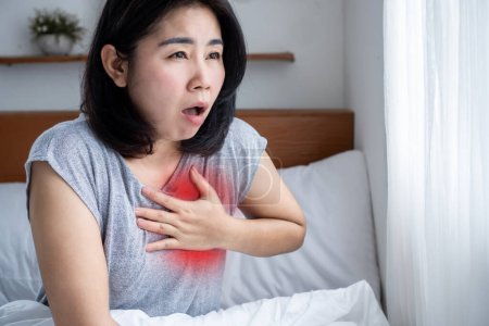 Enfermedad arterial coronaria concepto CAD con mujer asiática que sufre de dolor de pecho, dificultad para respirar y ataque cardíaco en la cama