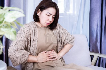 Asian woman suffering from stomachache and discomfort due to food poisoning 