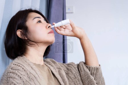 Photo for Close up Asian woman treating a runny nose with nasal spray for rhinitis, sinusitis, cold, and flu symptoms - Royalty Free Image