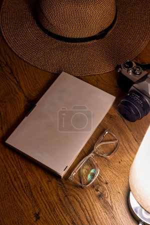 Téléchargez les photos : Un bureau d'explorateur en chêne orné de trésors vintage. Un chapeau classique, des verres intemporels, un livre vieilli et un appareil photo vintage sont magnifiquement disposés, baignés dans la lueur chaude d'une lampe de table - en image libre de droit