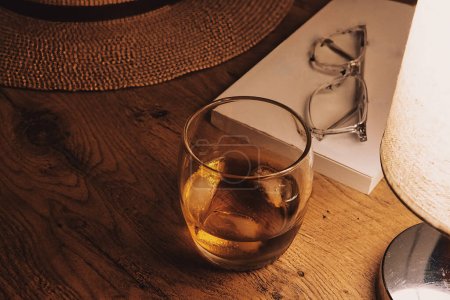 Téléchargez les photos : Bureau en chêne orné d'un verre de whisky, une ouverture, et la lueur ambiante d'une lampe de table - en image libre de droit