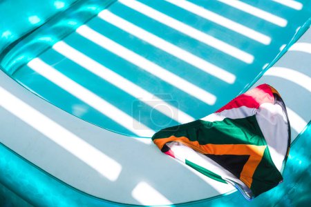 a pair of colorful swimming trunks laid by the side of a refreshing turquoise paddling pool on a bright sunny day
