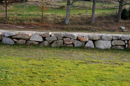 Trockenmauer dient als Terrassenterrasse für den Garten, wo sie eine Masse Erde hält. Die Wand ist leicht gewölbt, wodurch sie sich besser stabilisiert. Pflanzen von Stauden und Steingarten, Allee, Wiese