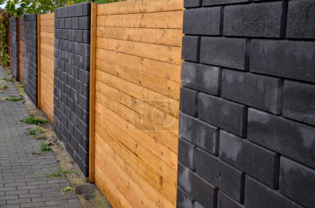 garden fencing where materials such as wood and rectangular concrete blocks are combined. between the walls are embedded pieces with planks. wet after rain