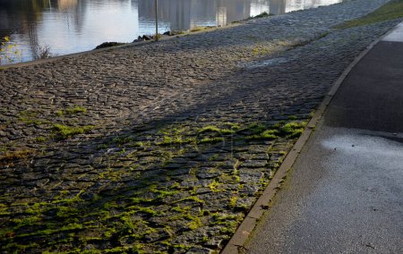 Photo for Edge of the river bank reinforced with giant stones as a breakwater against erosion of stone paving at the dock cobblestone promenade, moss covered, riverside - Royalty Free Image