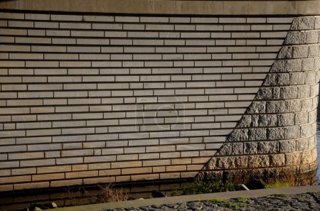 Téléchargez les photos : La combinaison d'un mur de pierre de taille lisse en bandes longitudinales suit l'arc de blocs de granit rugueux. pilier, clôture de la construction de brouillards et murs de soutènement de pierre. tailleur de pierre local - en image libre de droit