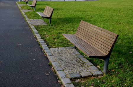 Photo for Walking path through park where there is also a bowling court made of a beige sandy surface in shape of a rectangle. a number of benches without backrests used to relax audience, wooden plank curbs - Royalty Free Image