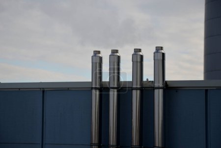 Photo for Industrial white building with sheet metal facade of repeating rectangle paneling. on wall are two silver-shiny chimney pipes with a curved and bevelled stainless steel pipe. gas heating turbo boiler - Royalty Free Image