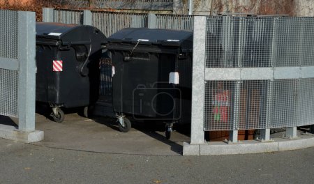 Photo for Yard for placing containers for sorting household waste. gray door and halving of perforated metal grid, expanded metal. stone wire baskets filled and sunk into grassy slope. reclining place - Royalty Free Image