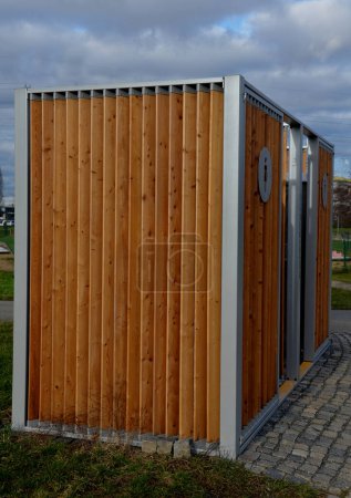 Photo for Closing cage for placing chemical toilets. unsightly plastic boxes are inside a metal house with a flat roof and wooden slats on the walls. athletes in park or mothers with children can pee, wash hand - Royalty Free Image