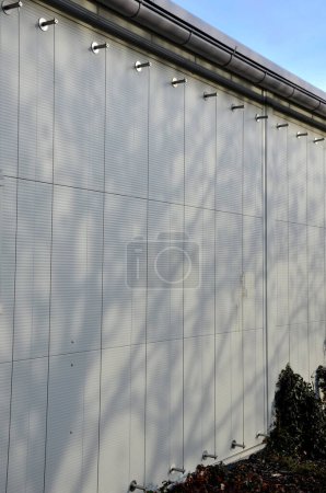 Téléchargez les photos : The sheet metal wall of the warehouse is improved with stainless steel cable holders for climbing plants. trellises made of stainless steel vertical cables. in a narrow strip of flowerbed covered - en image libre de droit