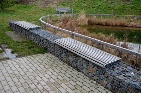 Téléchargez les photos : Swimming lake landscaped coastal zone of shallow water and a deeper part for swimming. fenced with wooden beams fence and gabion wall with plank benches. retention pond, tank, source, fire, dry - en image libre de droit