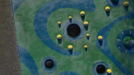 Foto de Superficie de goma azul de un patio de recreo con cucharadas amarillas y manchas de colores en las heladas de las huellas humanas. lentes elevadas como bolas, bancos de madera y trampolines circulares hundidos en el terreno. - Imagen libre de derechos