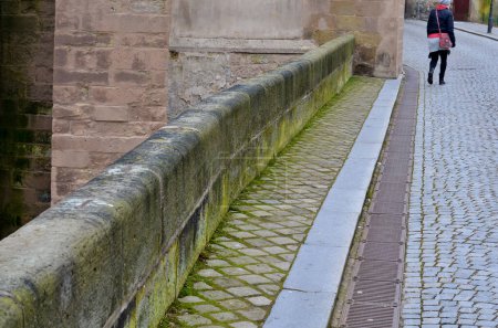 Photo for Stone balustrade of the bridge at the church made of worked sandstone blocks with a rounded edge. along the paved road is a metal grid of a longitudinal gutter for rainwater - Royalty Free Image