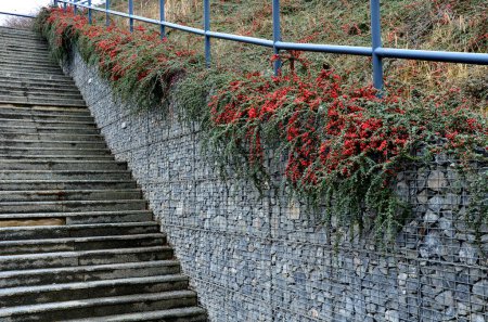 Bau einer steilen Treppe beim Steinmauer-Parkplatz mit hoher Haltbarkeit auch unter schwerer Last verzinktem Stahlbodenrost und Geländer. Gabionen über ihm ein Maschendrahtzaun. Korridor, eng