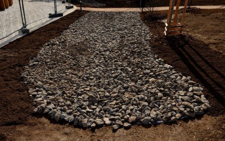 Photo for Delivery of gray river pebbles like mulch to flower beds in the garden using a wheelbarow from the body of a truck or trailer. shovel and rake the layer over the black nonwoven fabric. dirt road - Royalty Free Image