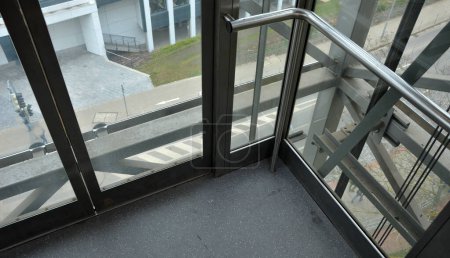 Photo for Riding an outdoor elevator with glass walls can be stressful for people who suffer from vertigo from heights. the boy is holding on to the pipe handrail - Royalty Free Image