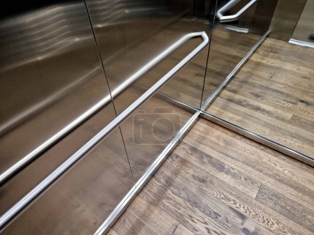 Photo for Stainless steel elevator cabin interior with hardwood oak floor and mirror paneling. handrail and reclining seat for seniors and relaxation in luxury offices, wood, wooden - Royalty Free Image