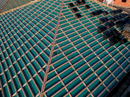 Photo for Finishing the laying of the roof covering from burnt cement tiles. stacks laid out on board battens. construction worker work environment. pride and finish the house soon, green foil, vapour, barrier - Royalty Free Image
