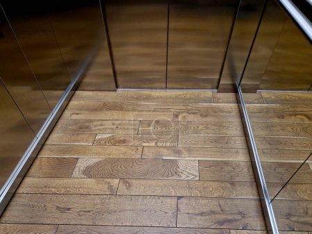 Téléchargez les photos : Intérieur de la cabine de l'ascenseur en acier inoxydable avec parquet en chêne et lambris miroir. main courante et siège inclinable pour personnes âgées et détente dans les bureaux de luxe, bois, bois - en image libre de droit