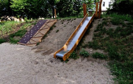 double shiny stainless steel slide on the playground. a hill lined with wooden logs used as palisades. autumn day park. it resembles a rocky slope, palisade, palissade, slope, hill, terrace, above