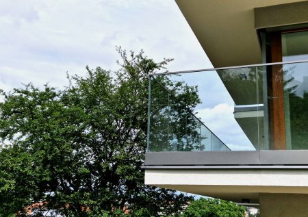 Geländer eines Luxushauses, das aus Glaspaneelen besteht, die mit Metallgriffen aus Edelstahl befestigt sind. vermittelt einen luftigen Eindruck. Abdeckung aus poliertem Metall auf einem Fenster der Gewächshausterrasse, Reflexion