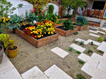 Photo for Corner of the family garden with several beds bordered by boards. there is compacted sand around and the paving irregularly jaggedly rises into the mortar. flowering beds with annuals - Royalty Free Image