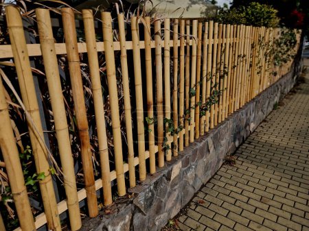 Photo for The fence around the house is made of split bamboo. half logs screwed to the board. the grass is dry and durable. elements of Japanese Asian style at the house - Royalty Free Image
