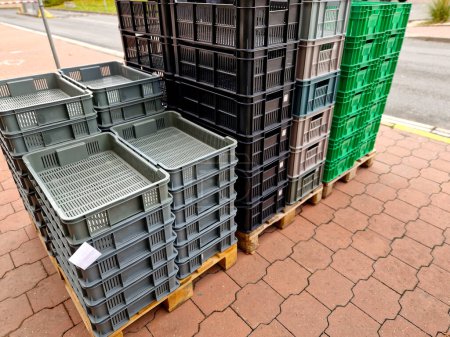 Foto de Pilas de cajas de verduras y otros almacenamientos están en el pavimento frente a una tienda de mejoras para el hogar. almacén de una empresa de alimentos con cajas de plástico apiladas gato palet - Imagen libre de derechos