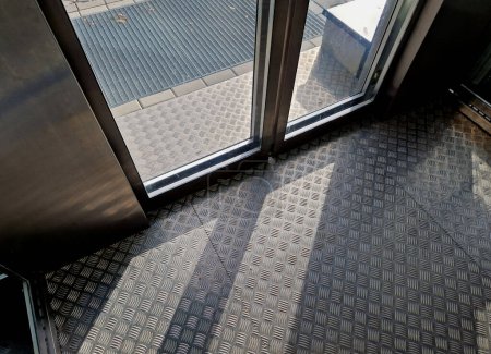 Téléchargez les photos : Ascenseur extérieur avec plancher antidérapant en métal déployé. grille métallique maille chaussures tapis de nettoyage. intérieur, ensoleillé, sol, façade extérieure - en image libre de droit