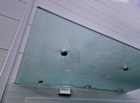 Toiture en verre au-dessus de l'entrée bâtiment industriel avec revêtement métallique de façade. panneau de verre à paroi épaisse pend au-dessus de la porte sur des tiges métalliques avec des supports de cibles rondes, givré, acier inoxydable, bleu